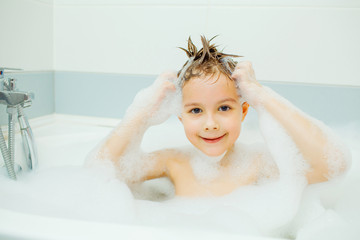 Happy young boy taking a bath in the foam.. Smiling child washes his head with shampoo.