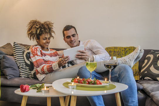 Couple relaxing together in sofa with tablet computer pc having fun. Romantic young happy multiracial couple in love sitting at home in sofa resting having fun maybe watching movie. Man and woman.