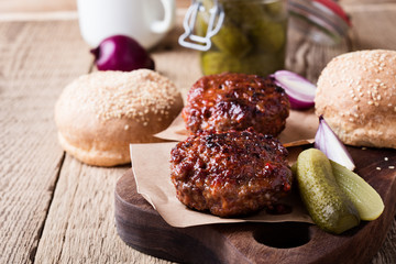 Cooked beef burger, buns and pickles on wooden table