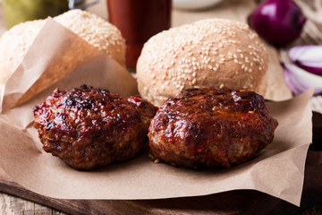 Cooked beef burger, buns and pickles on wooden table