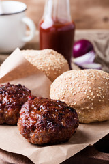 Cooked beef burger, buns and pickles on wooden table