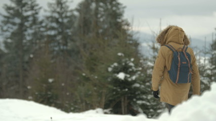 Fototapeta premium man goes through the snowy winter forest in a brown jacket with a hood and a backpack