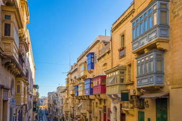 Fototapeta na wymiar Valletta, Malta - Typical narrow street with colorful traditional windows and balconies and clear blue sky on a summer day