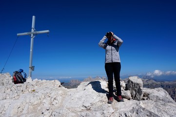 Obraz premium Wanderin erkundet Umgebung mit Fernglas neben Gipfelkreuz 