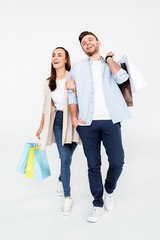 Full length view of happy young couple walking with shopping bags on white