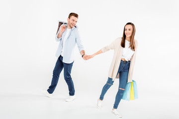 Fototapeta premium Happy young couple with shopping bags holding hands on white