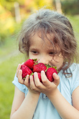 Portrait of small smiling girl with a  handful of just gathered big strawberries in a garden