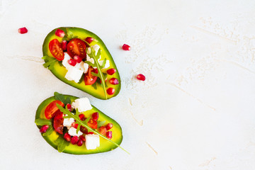 Healthy organic vegetarian diet food, avocado with pomegranate seeds, feta cheese, arugula leaves and cherry tomatoes on the table, top view.