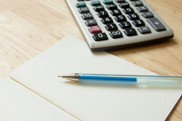 Calculator, pen, blank note book on wood table