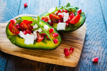 Healthy organic vegetarian diet food, avocado with pomegranate seeds, feta cheese, arugula leaves and cherry tomatoes on wooden table, closeup.