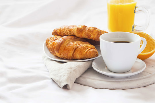 Bed breakfast with coffee cup, croissants and orange juice on white sheets