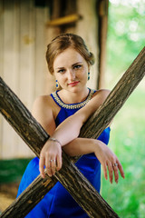 Young overweight girl at blue dress posed background spring garden on wooden hut.