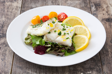 Fried cod fillet and salad in plate on wooden background
