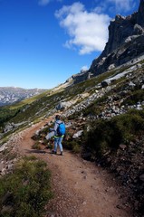 Fototapeta premium Wanderin unterwegs mit Rucksack und Stöcken auf Weg entlang Felshang / Rosengarten Schlern Naturpark