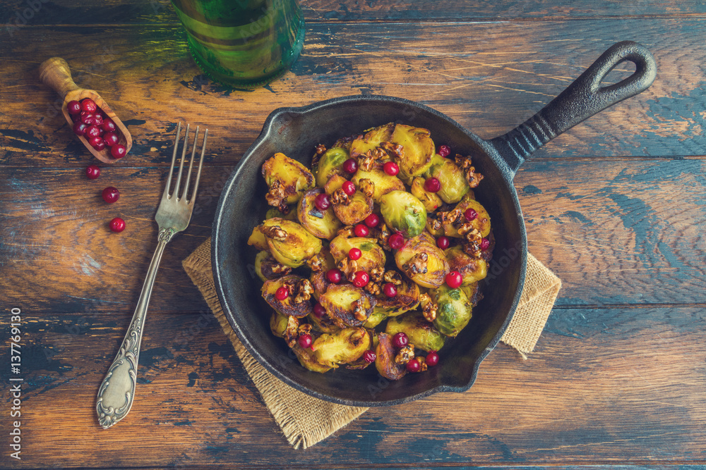 Wall mural roasted brussels sprouts with caramelized walnuts and cranberries in a cast iron frying pan on a woo - Wall murals
