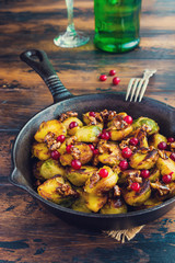Roasted Brussels sprouts with caramelized walnuts and cranberries in a cast iron frying pan on a wooden table.