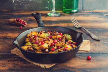 Roasted Brussels sprouts with caramelized walnuts and cranberries in a cast iron frying pan on a wooden table.