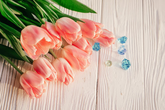 beautiful pink tulips with blue gemstones on white rustic wooden background. tender view of spring flowers in soft morning sunny light with space for text. blogging advertising concept