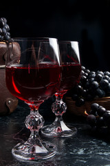 Glass of red wine on dark marble background. Cluster of blue grapes on on back background..