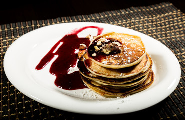 Homemade sweet pancakes with fruit jam on a white plate. Breakfast with stack topped blueberry jam and walnuts.