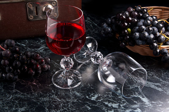 Glass of red wine on dark marble background. Cluster of blue grapes on on back background.