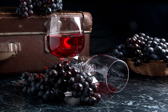 Glass of red wine on dark marble background. Cluster of blue grapes on on back background.