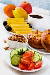 Breakfast on the table, salad from fresh tomatoes and cucumbers, almond nuts, bread, cheese, black olives, cup of coffee and fruits.