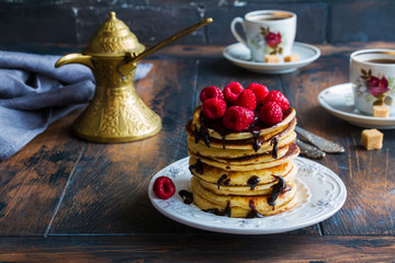 Stack of homemade pancakes with raspberries and chocolate, vintage white plate, Turkish coffee pot,...