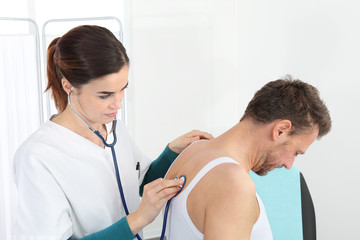 Doctor examining patient with stethoscope in medical office