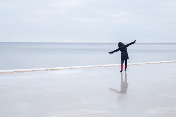 Young woman on the ice at the seashore feels the freedom in winter afternoon.