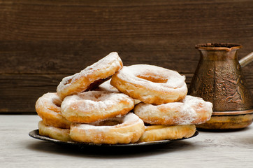 Donuts sprinkled with powdered sugar, coffee pots, dark wood background. Close-up, side view