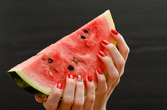 Large slice of ripe watermelon in female hands on a black background, close up