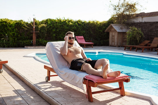 Young handsome man sunbathing, lying on chaise near swimming pool.