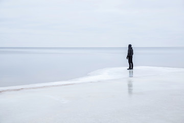 Young man on the ice at the seashore feels the freedom in winter afternoon.