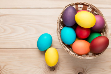 Two Easter eggs near a wicker basket of eggs on the wooden table