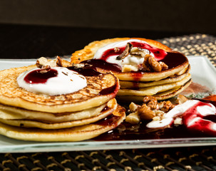 Homemade sweet pancakes with fruit jam, sour cream on a white plate. Breakfast with stack topped blueberry jam and walnuts.