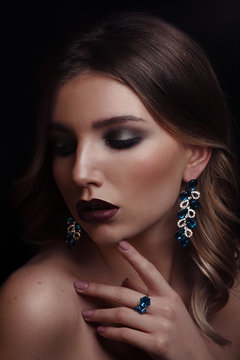 Studio beauty portrait of young woman wearing ring and earrings with blue gemstones on black background Add noise
