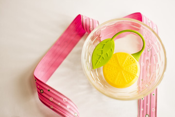 Yellow lemon lies in a vase. Vase standing on a white background. On a white background is a pink ribbon. The picture creates a good mood.