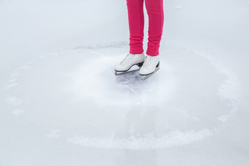 Woman skating with white skates on the ice area at the seashore in winter day. Weekends activities outdoor in cold weather.