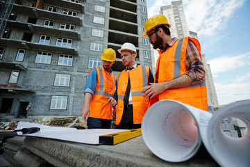 Low angle portrait of two workmen showing apartment building blueprints to inspector on...