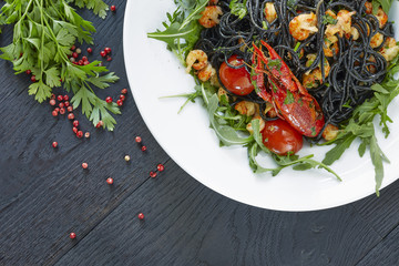 Black spaghetti with crayfish, fresh green arugula, cilantro, pepper and olive oil on a dark wooden table. 