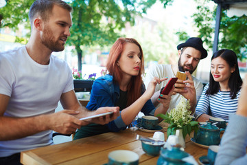 Group of modern teenagers with gadgets sitting in cafe