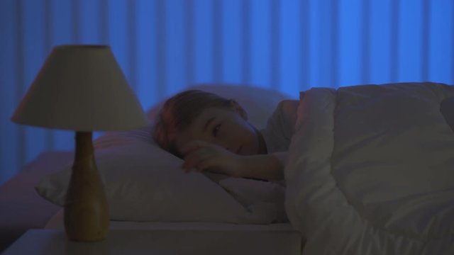 The sleeping girl turn on the lamp. Evening night time