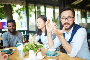 Asian man in eyeglasses talking to one of friends