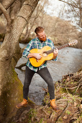 Hipster man with red beard with a guitar in the field