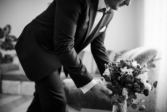Groom with wedding bouquet at his room at morning day. Black and white photo