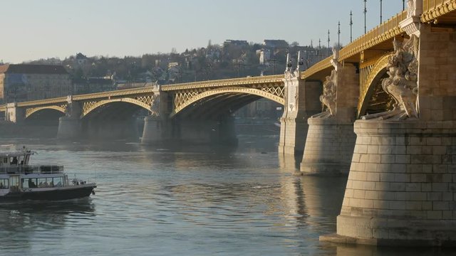 Nice view of the Danube and the Margit Bridge lit by the soft evening sun in Budapest. On the river excursion boat floats.

