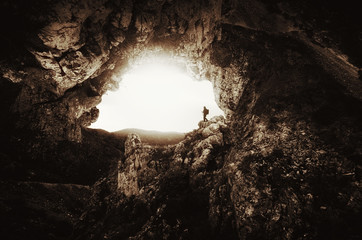 big cave entrance with man silhouette on cliff