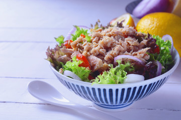 tuna fish salad with lettuce, onion, lemon and tomatoes on white wooden table in background.