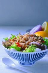 tuna fish salad with lettuce, onion, lemon and tomatoes on white wooden table in background.